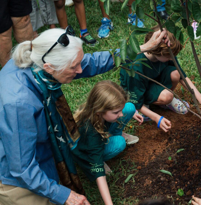 Dr. Jane Goodall helps two children plant a tree in the ground
