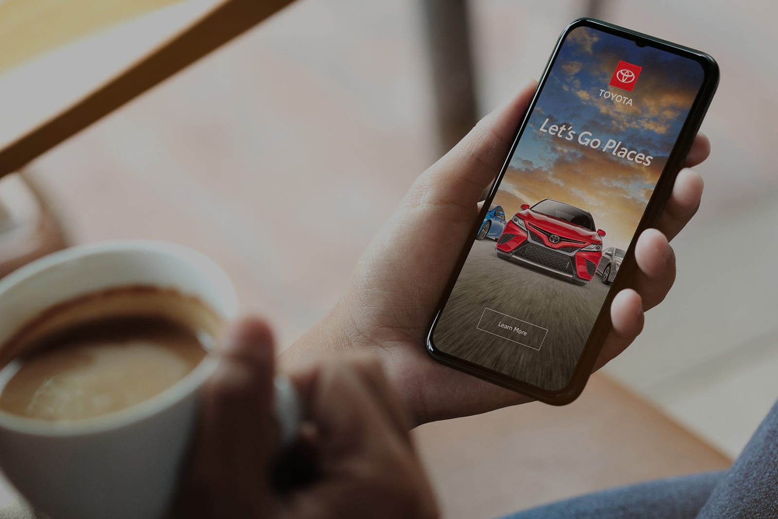 Hands holding cup of coffee and phone with Toyota branding