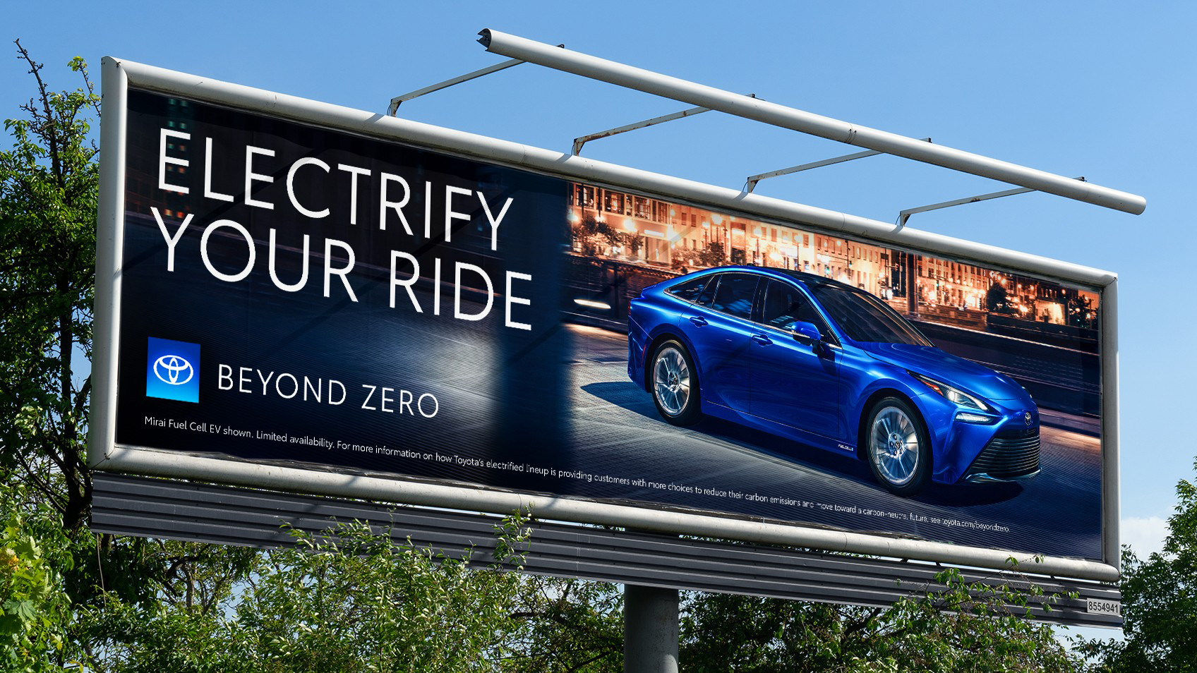 Beyond Zero billboard ad with sky and trees in background. The ad shows a blue Mirai with the headline “Electrify Your Ride” with the Beyond Zero logo bottom left and disclaimer below.