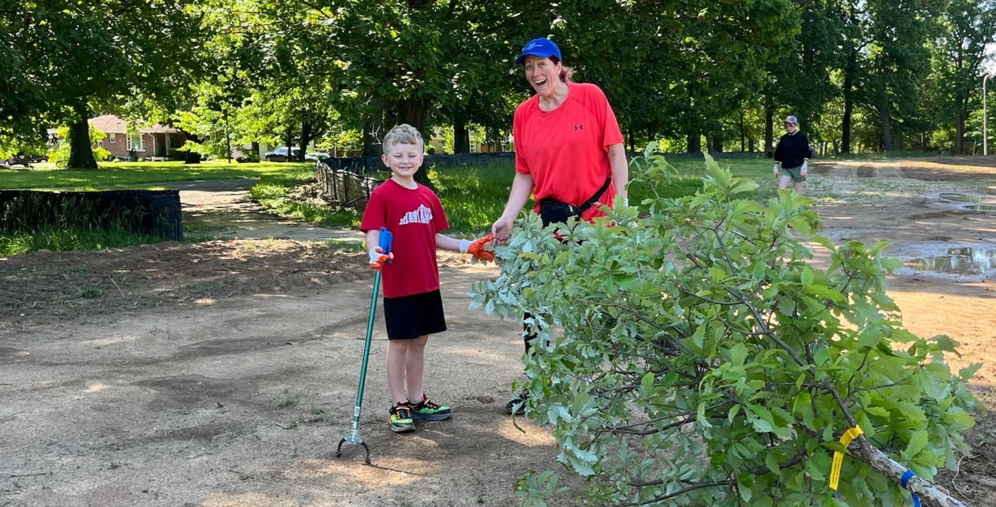 Two volunteers, a woman and child, standing in front of a tree getting ready to be planted,