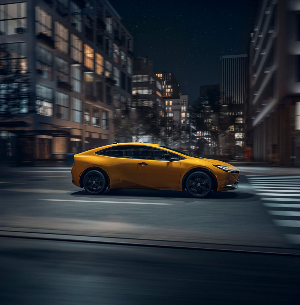 Photo of a yellow 2026 Prius driving down a street at night