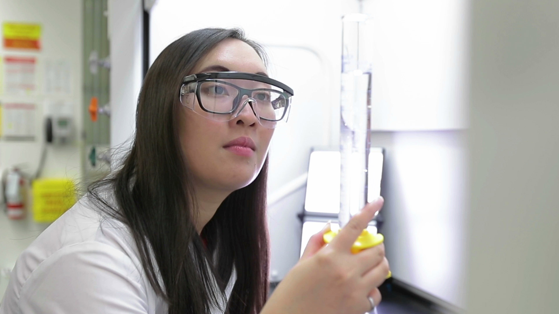 Scientist in white lab coat inspects liquid in a beaker,